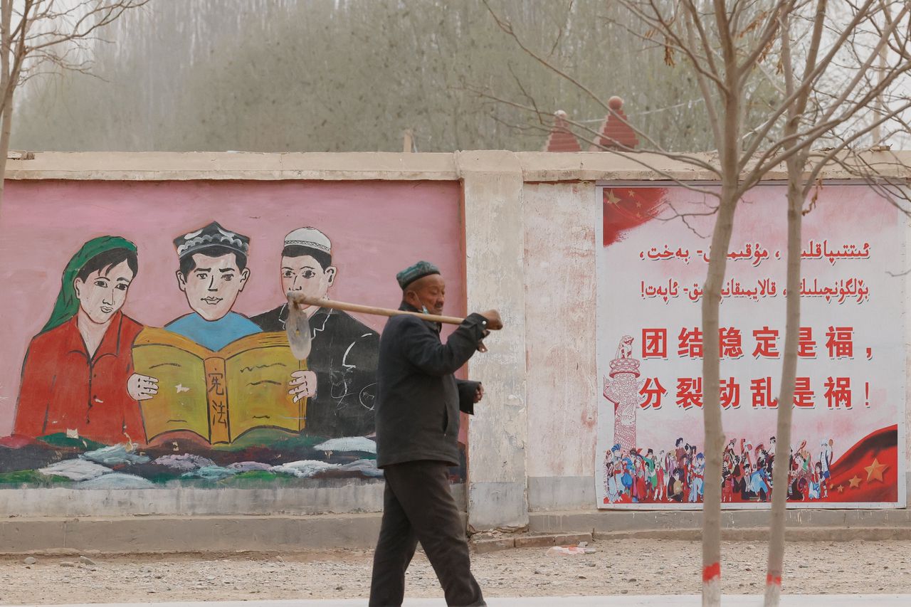 Een boer loopt langs regeringspropaganda waarin inwoners van etnische minderheden de grondwet lezen met slogans als: ‘Eenheid en stabiliteit is geluk, separatisme en onrust is ongeluk’, in de buurt van Kashgar in de autonome regio Xinjiang in het noordwesten van China.