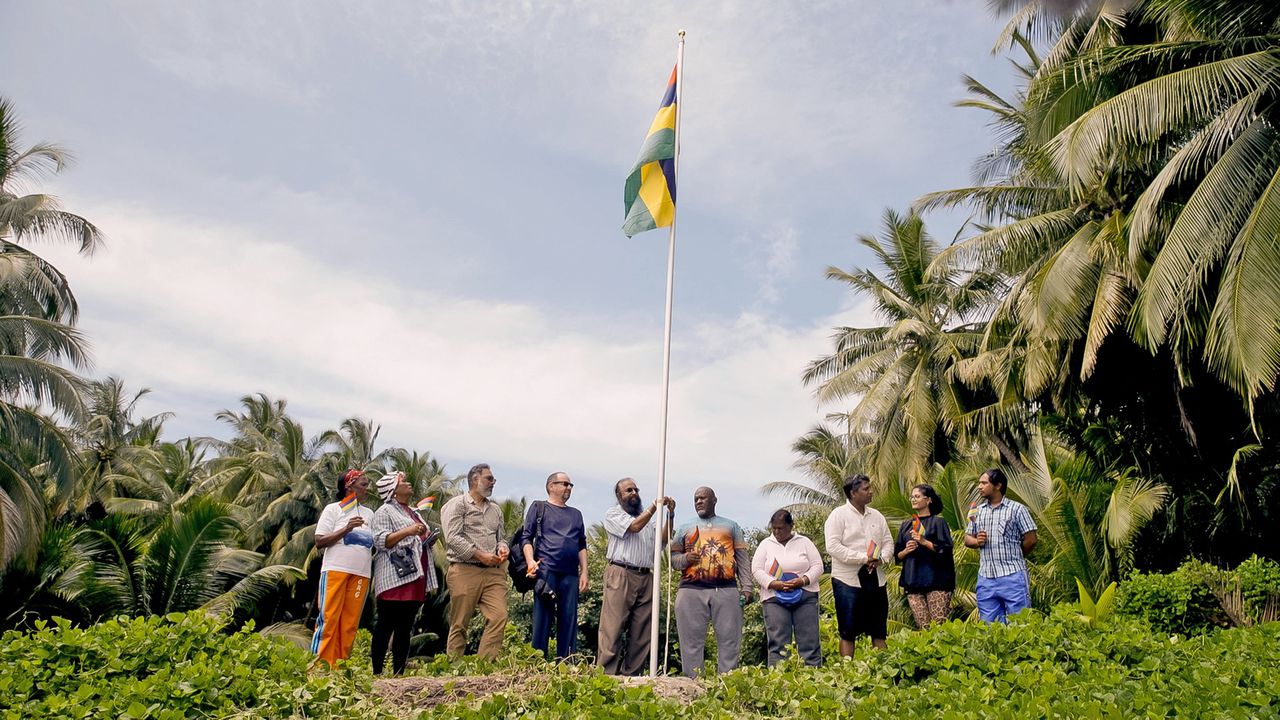 Oliver Bancoult (eerste rechts naast de vlag) hees samen met andere Chagossianen bij een bezoek vorig jaar de vlag van Mauritius op een van de eilanden.