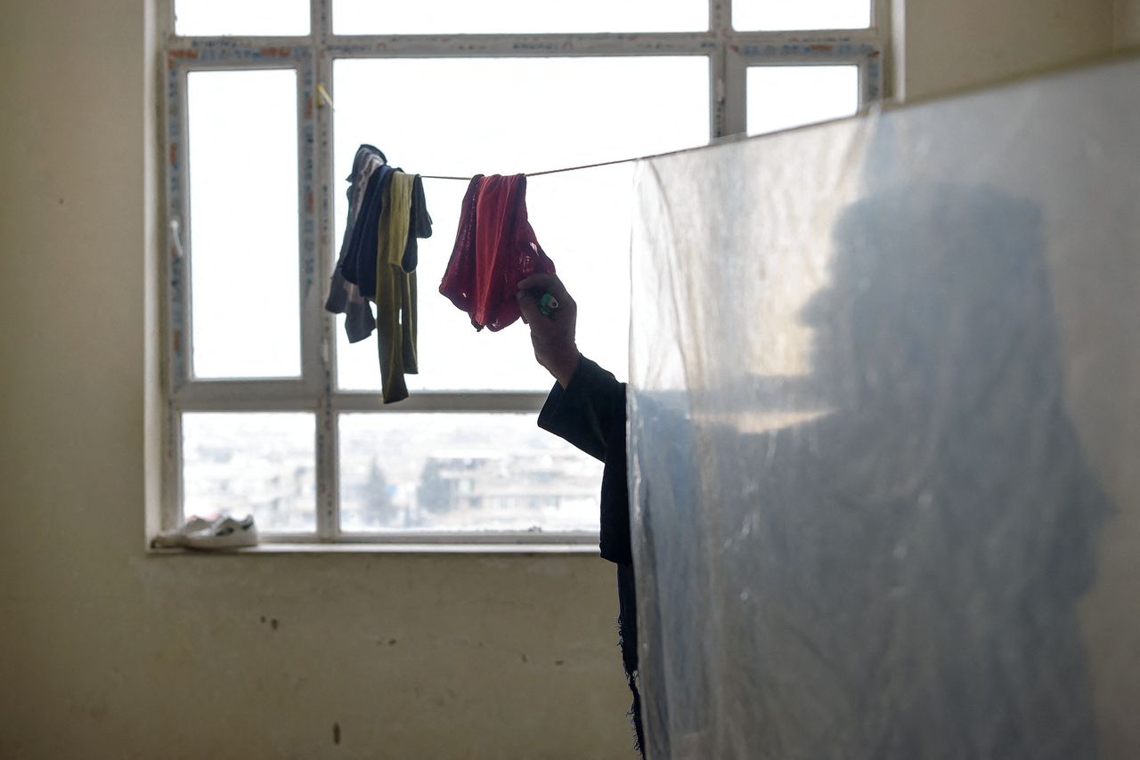 Een Afghaanse vrouw hangt kleren te drogen tijdens een interview met AFP in een huis op een geheime locatie in Afghanistan. Ze werd jarenlang misbruikt door haar ex-man, die al haar tanden brak. De Taliban maakten haar scheiding ongedaan.
