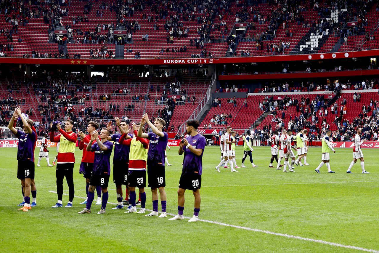 De spelers van AZ vieren in de Johan Cruijff Arena met de meegereisde fans de overwinning op Ajax, dat op de achtergrond een rondje langs de leeggestroomde tribunes loopt.